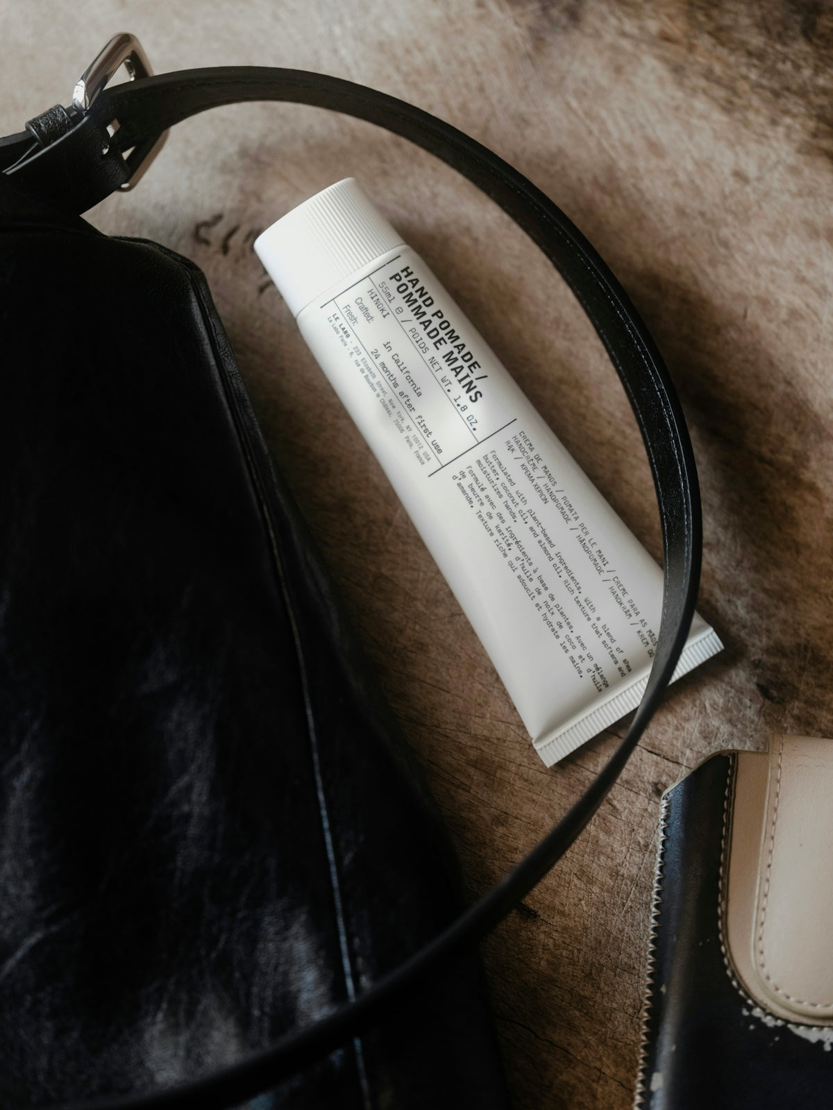 Hand cream tube rests on textured surface near bag.